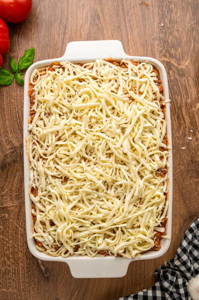 Shredded mozzarella on top of meat sauce in a casserole dish