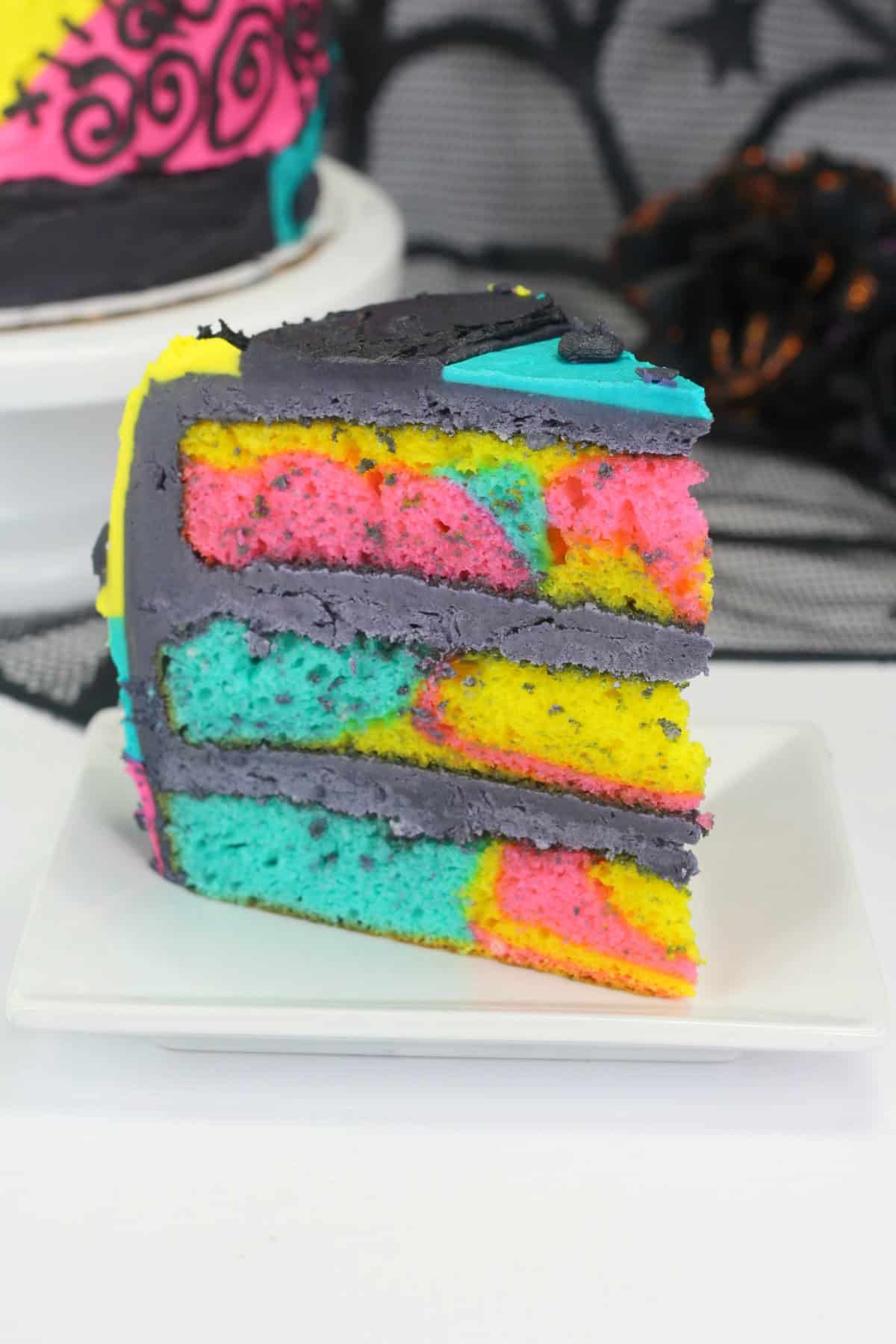 A slice of Sally Skellington Nightmare Before Christmas cake with vibrant tie-dye colors, set against a spider web-themed background.
