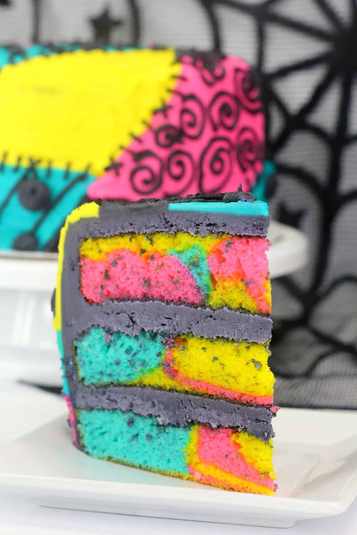 A slice of Sally Skellington Nightmare Before Christmas Cake  with vibrant layers of pink, yellow, and blue, decorated with patchwork designs from the "Nightmare Before Christmas" character.