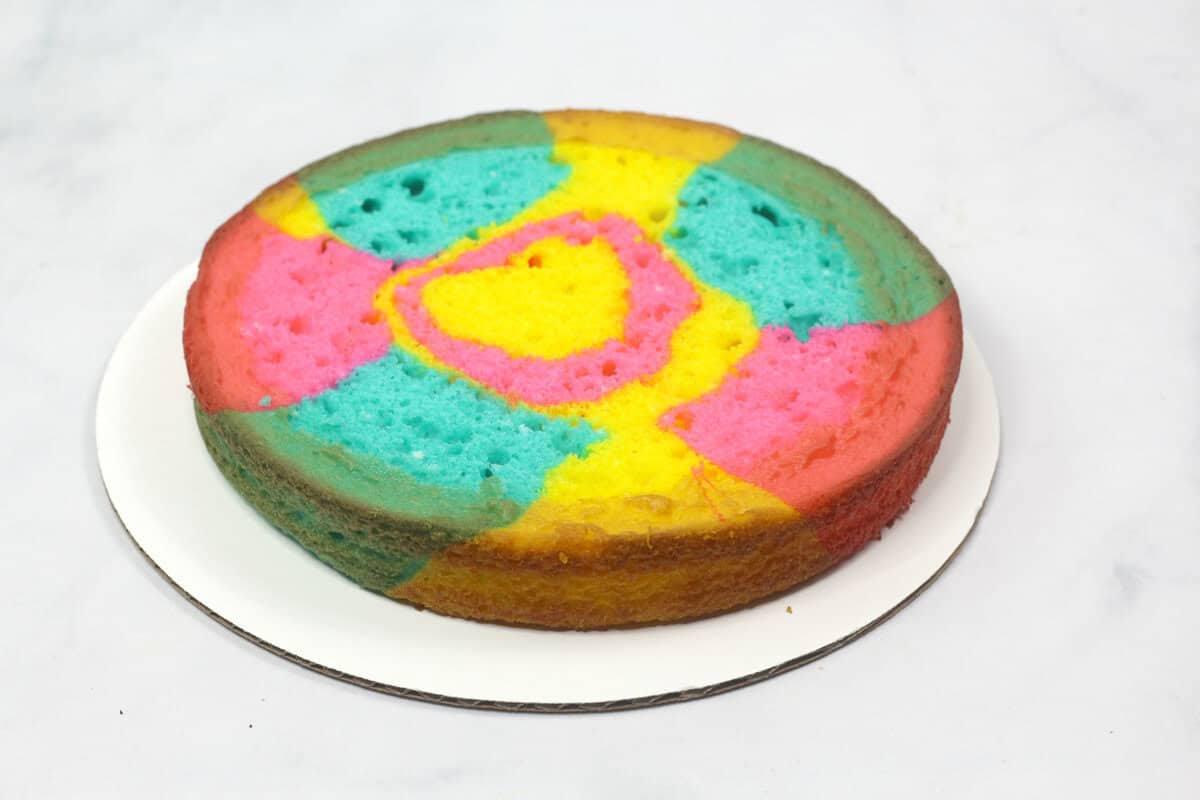 A freshly baked tie-dye cake layer with bright colors of pink, yellow, and blue before frosting is applied.