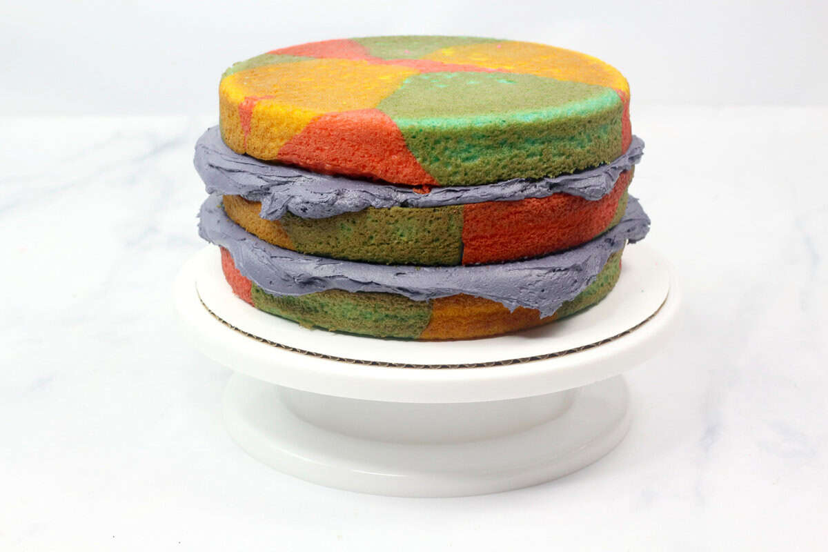 The stacked tie-dye cake layers with gray buttercream frosting between them, awaiting the outer decoration.