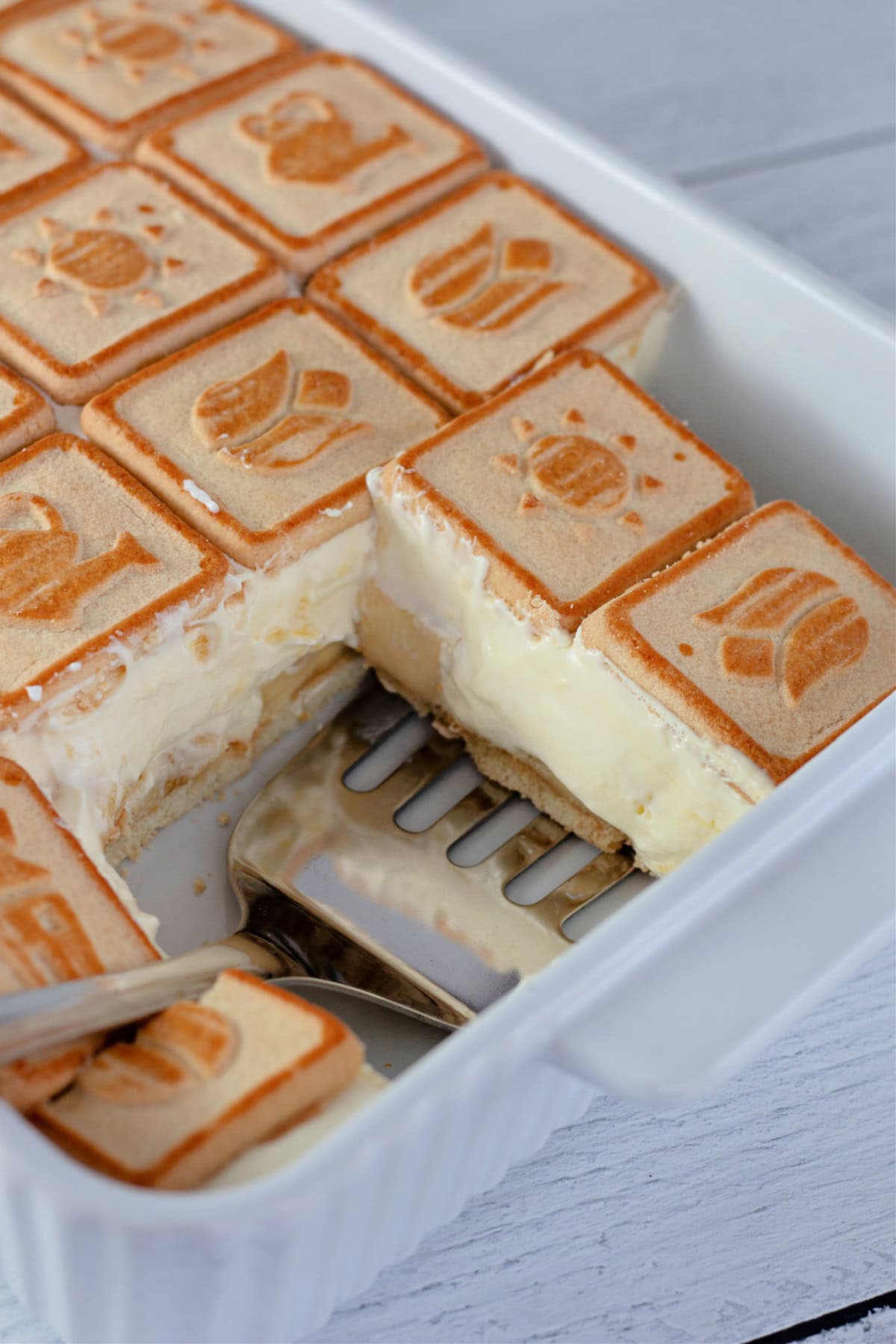 A close-up shot of a slice of banana pudding being lifted out of the baking dish, showing the creamy texture and layered cookies.