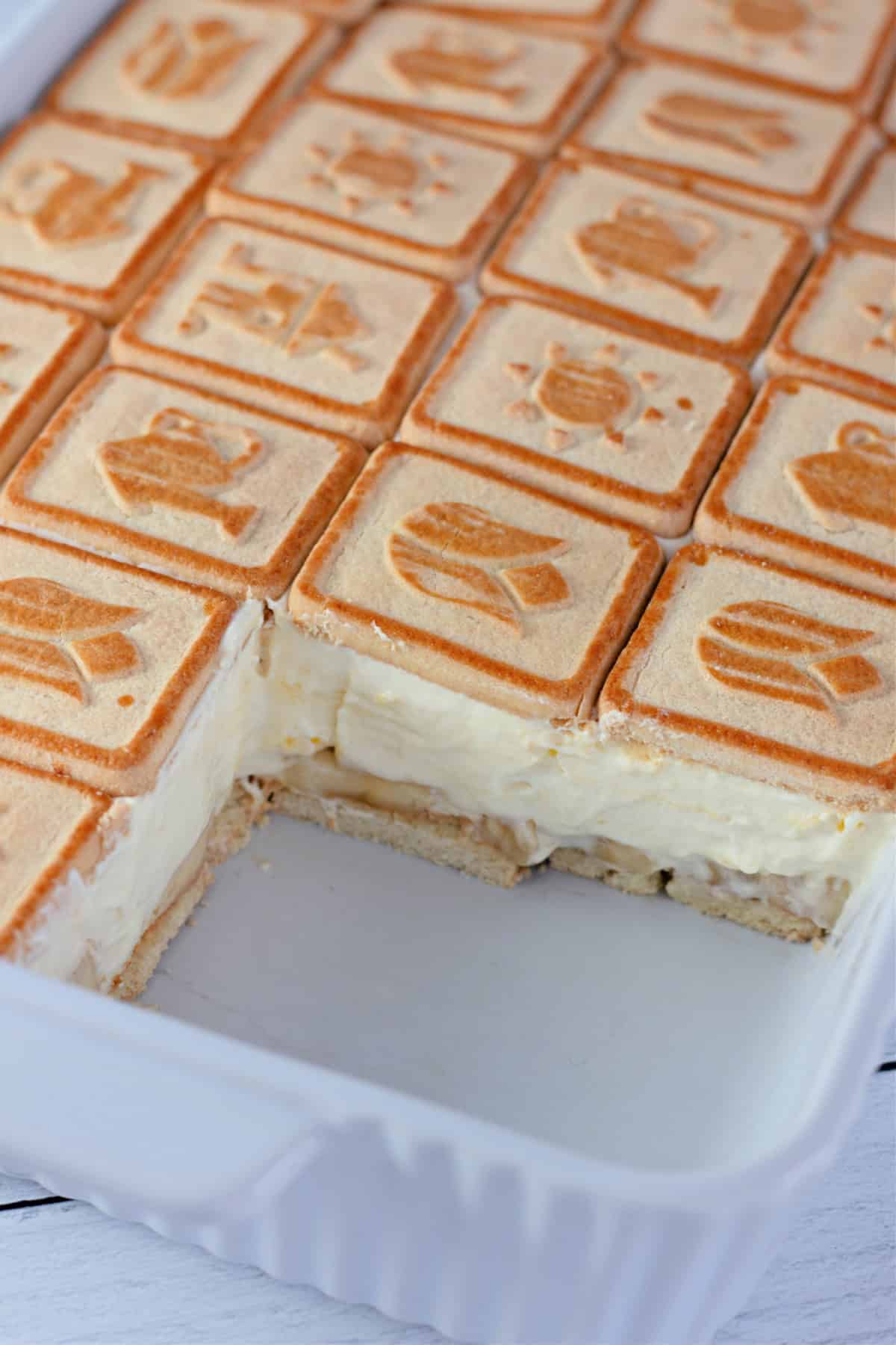 A baking dish of banana pudding with a portion removed, revealing the creamy layers of pudding, banana, and cookies.