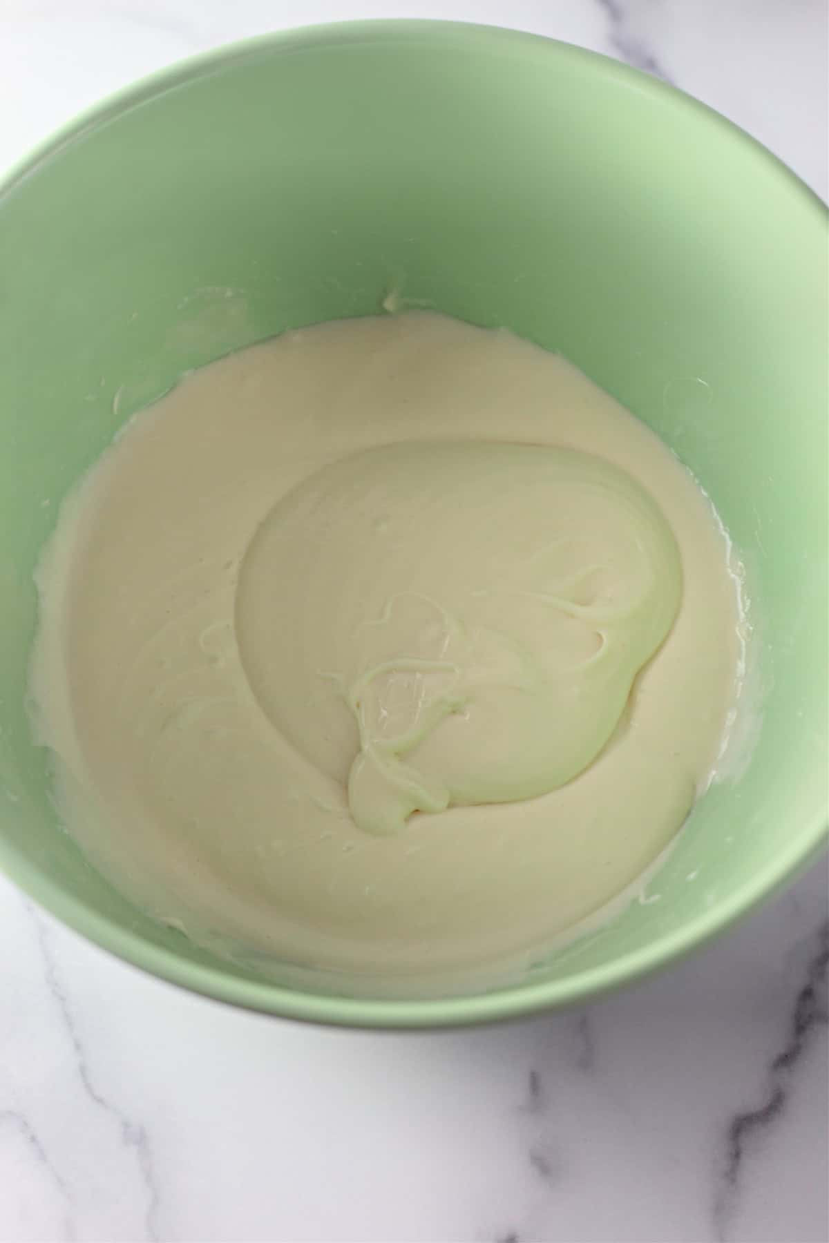 A green mixing bowl showing the smooth and creamy mixture for banana pudding.