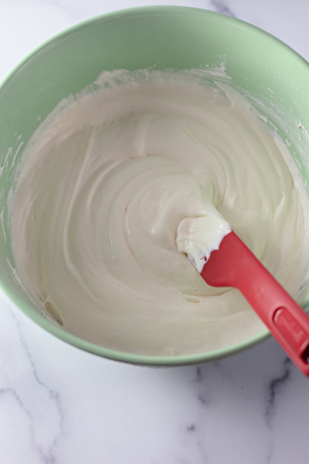 A green bowl with a creamy mixture of vanilla pudding and whipped cream cheese, ready for assembly.