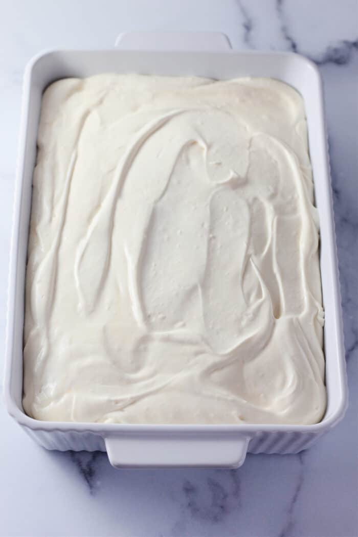 A white rectangular dish with a smooth layer of creamy pudding mixture spread evenly over the Chessmen Cookies.