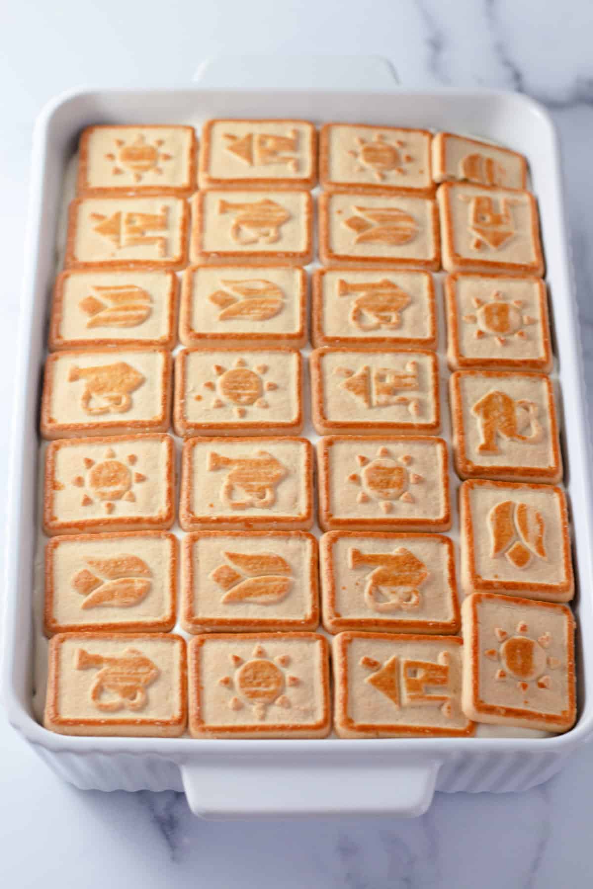 A white rectangular dish with a layer of Chessmen Cookies, laid out in rows for the final layer of banana pudding.