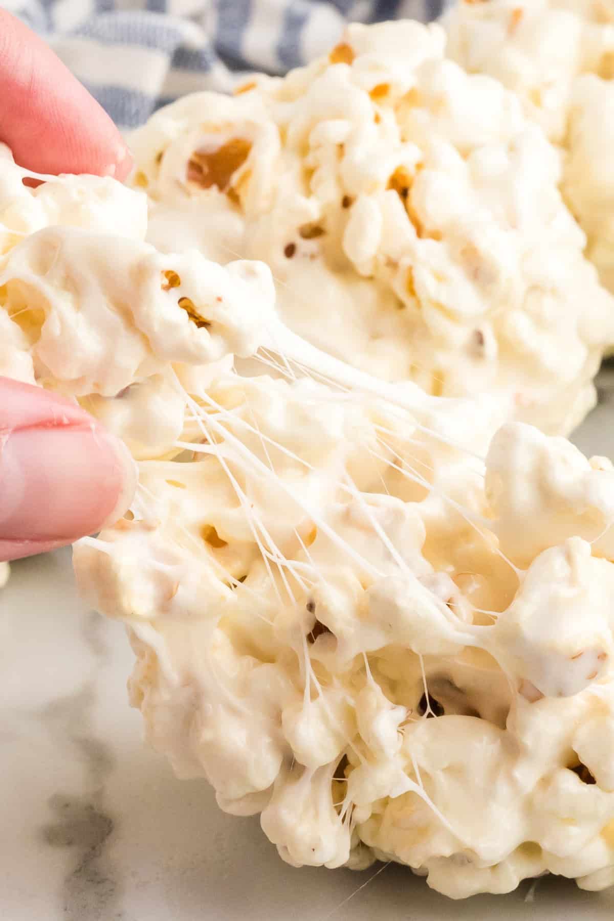 A person pulling apart a sticky popcorn ball, revealing gooey strands of melted marshmallow.