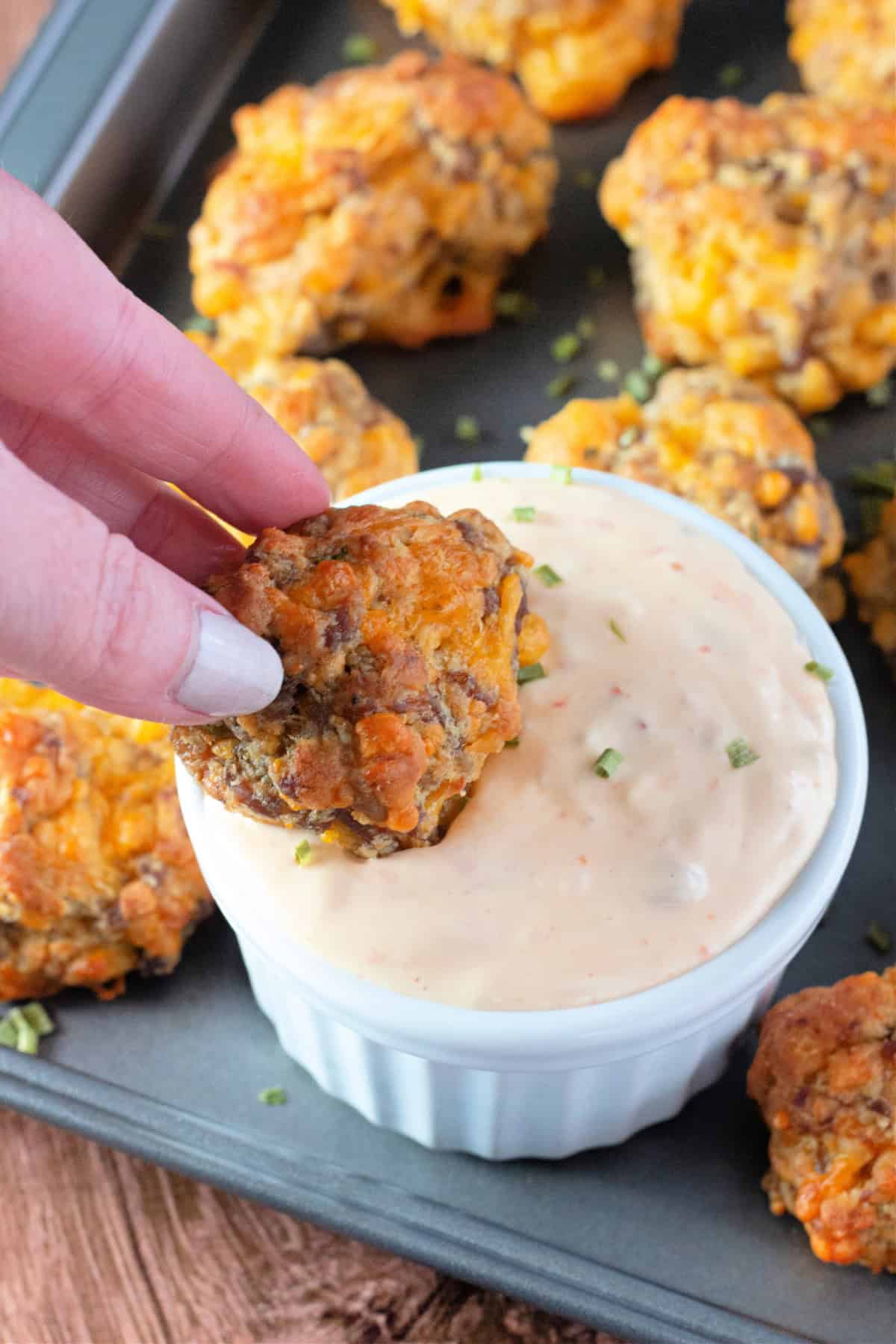 A hand holding a sausage ball with a bite taken out, revealing the cheesy and savory interior.