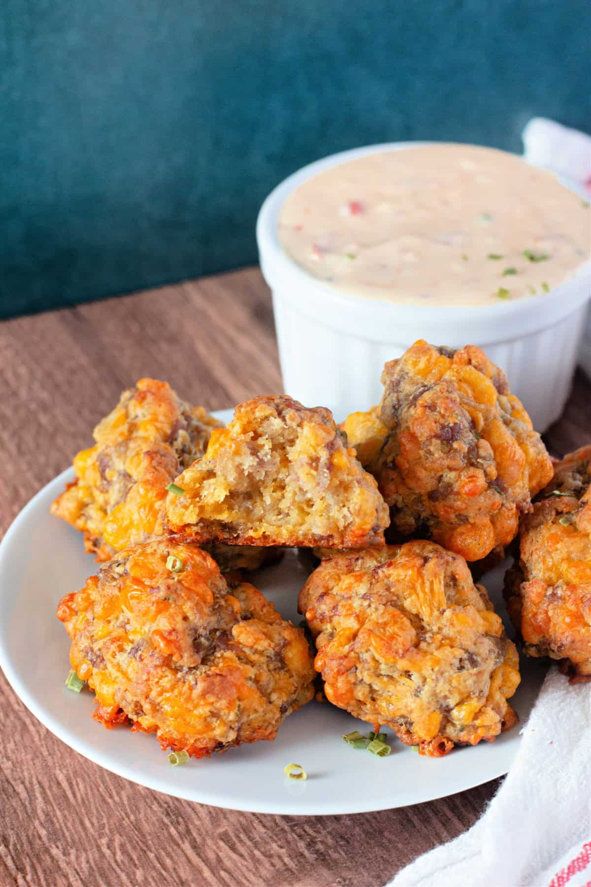 These Sausage Balls are just what you need! Whether you're craving a grab-and-go breakfast, a satisfying appetizer, or a hearty afternoon snack, these savory bites have you covered. Made with juicy sausage, sharp cheddar cheese, biscuit mix, fresh chives, and a splash of milk, they come together in minutes. Perfectly golden and packed with flavor, these sausage balls are a guaranteed hit for any occasion. A plate of golden, freshly baked sausage balls served with a small bowl of dipping sauce.