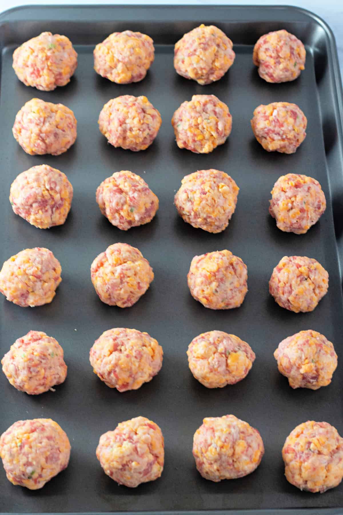 Uncooked sausage balls lined up on a baking sheet, ready to be baked.