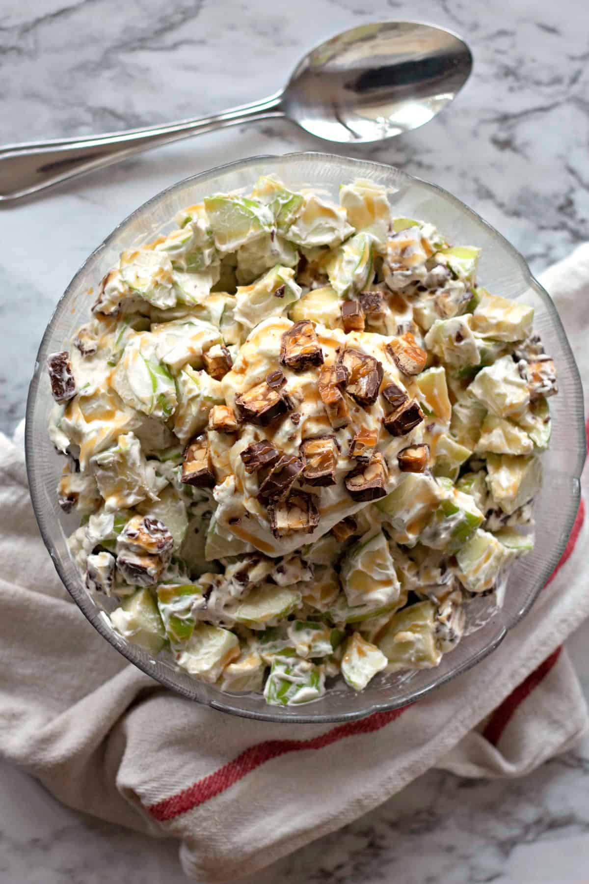 Overhead view of a bowl filled with Snickers Salad, featuring chopped Snickers bars and a creamy mixture of apples and dressing, with a garnish of Snickers pieces on top.