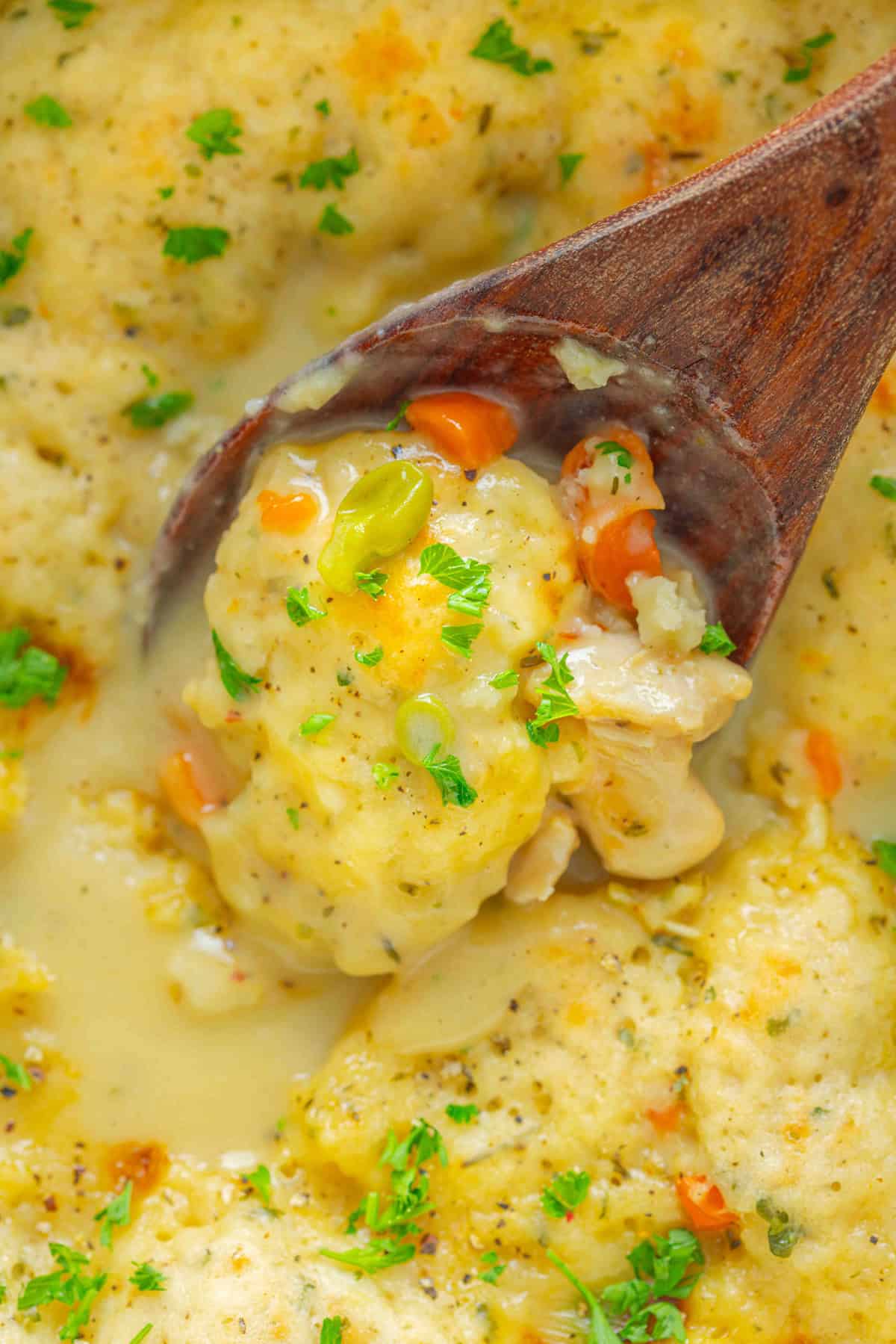 A wooden spoon stirring Bisquick chicken and dumplings