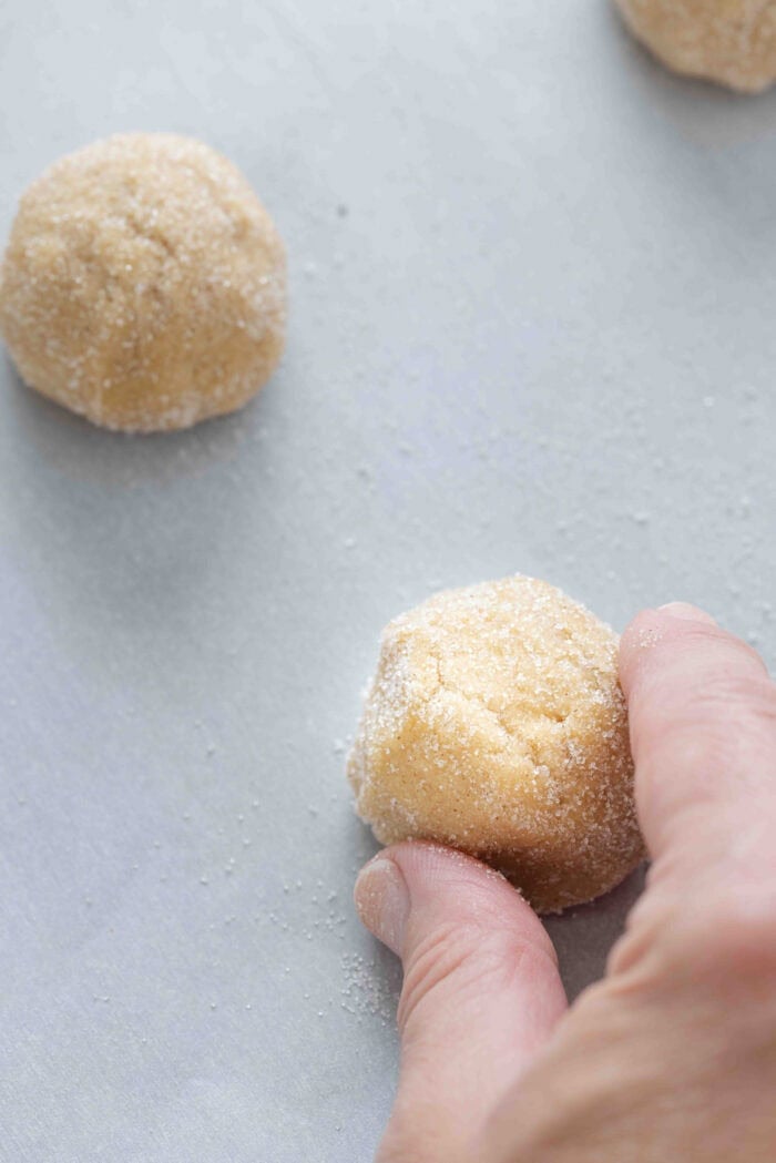 A hand placing a ball of cookie dough on a baking sheet
