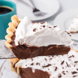 A close-up slice of rich chocolate cream pie topped with whipped cream and chocolate shavings, showing its smooth, creamy filling and flaky crust.