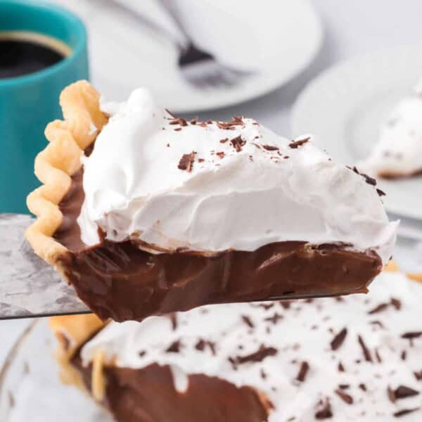 A close-up slice of rich chocolate cream pie topped with whipped cream and chocolate shavings, showing its smooth, creamy filling and flaky crust.