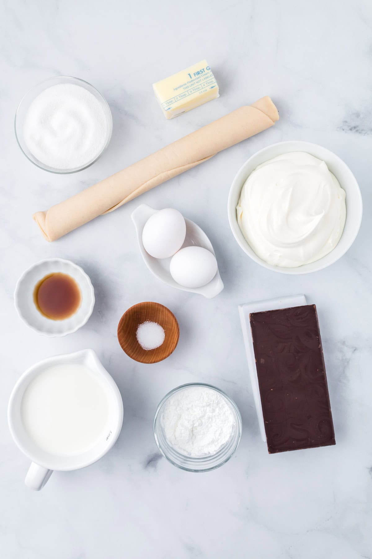 Ingredients for the chocolate cream pie, including sugar, butter, vanilla extract, eggs, pie crust, milk, cornstarch, salt, and a block of chocolate, neatly arranged on a marble surface.