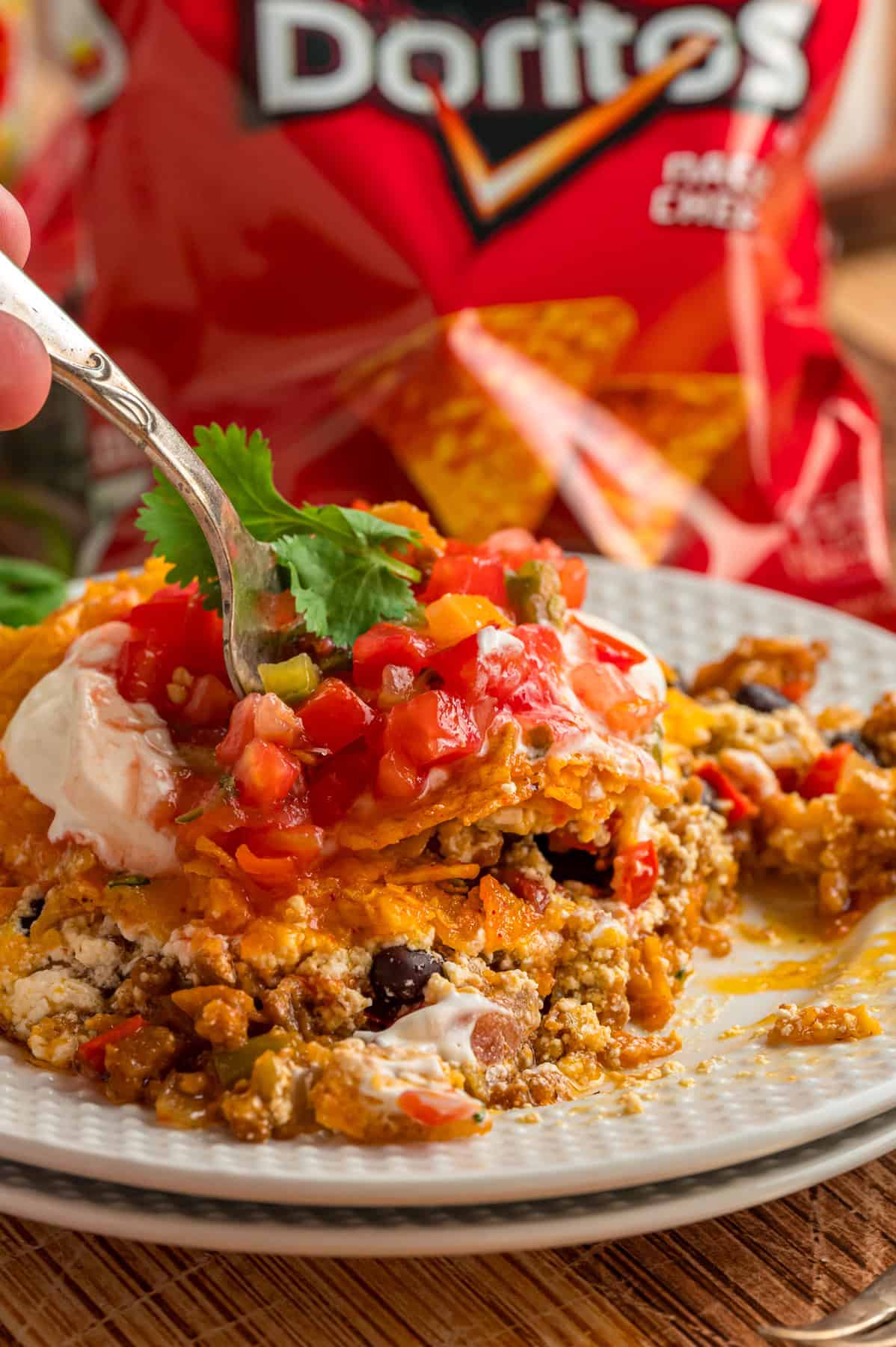 A fork diving into a plate of Dorito casserole topped with salsa
