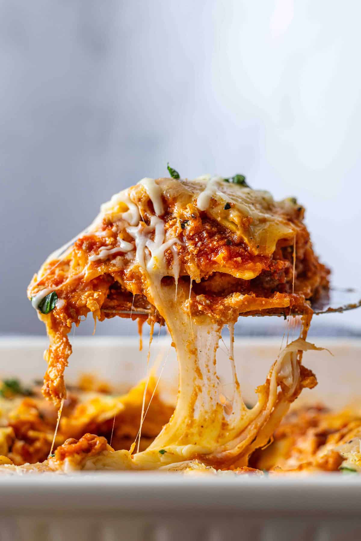 This Ravioli Lasagna recipe features layers of cheese ravioli, meat sauce, shredded cheese, and ricotta. Serve with garlic bread & salad. Lifting a serving of ravioli lasagna from the baking dish
