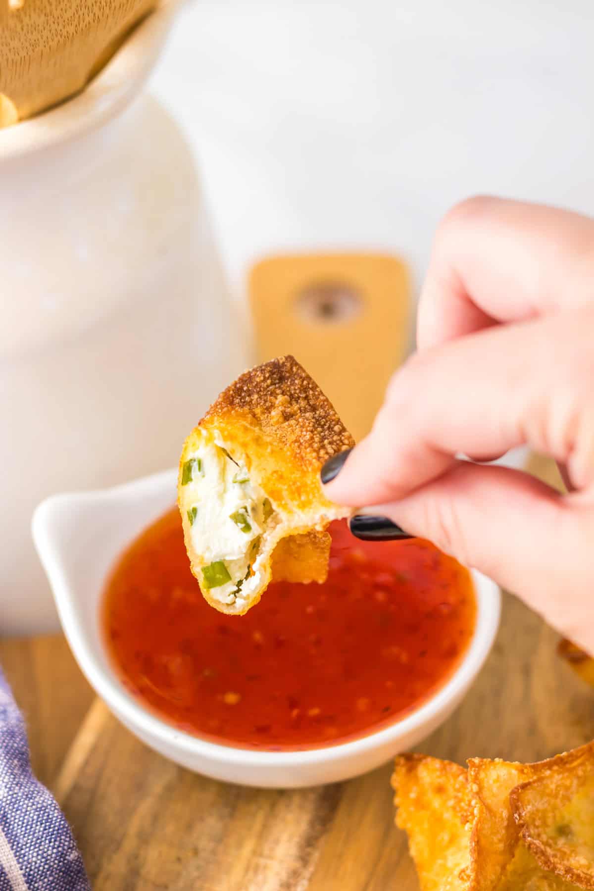 A hand dipping a cream cheese rangoon into a bowl of sweet chili sauce