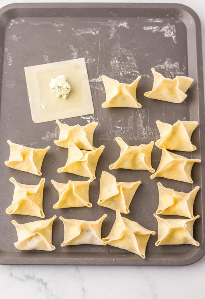 Wonton wrappers filled with cream cheese on a baking sheet