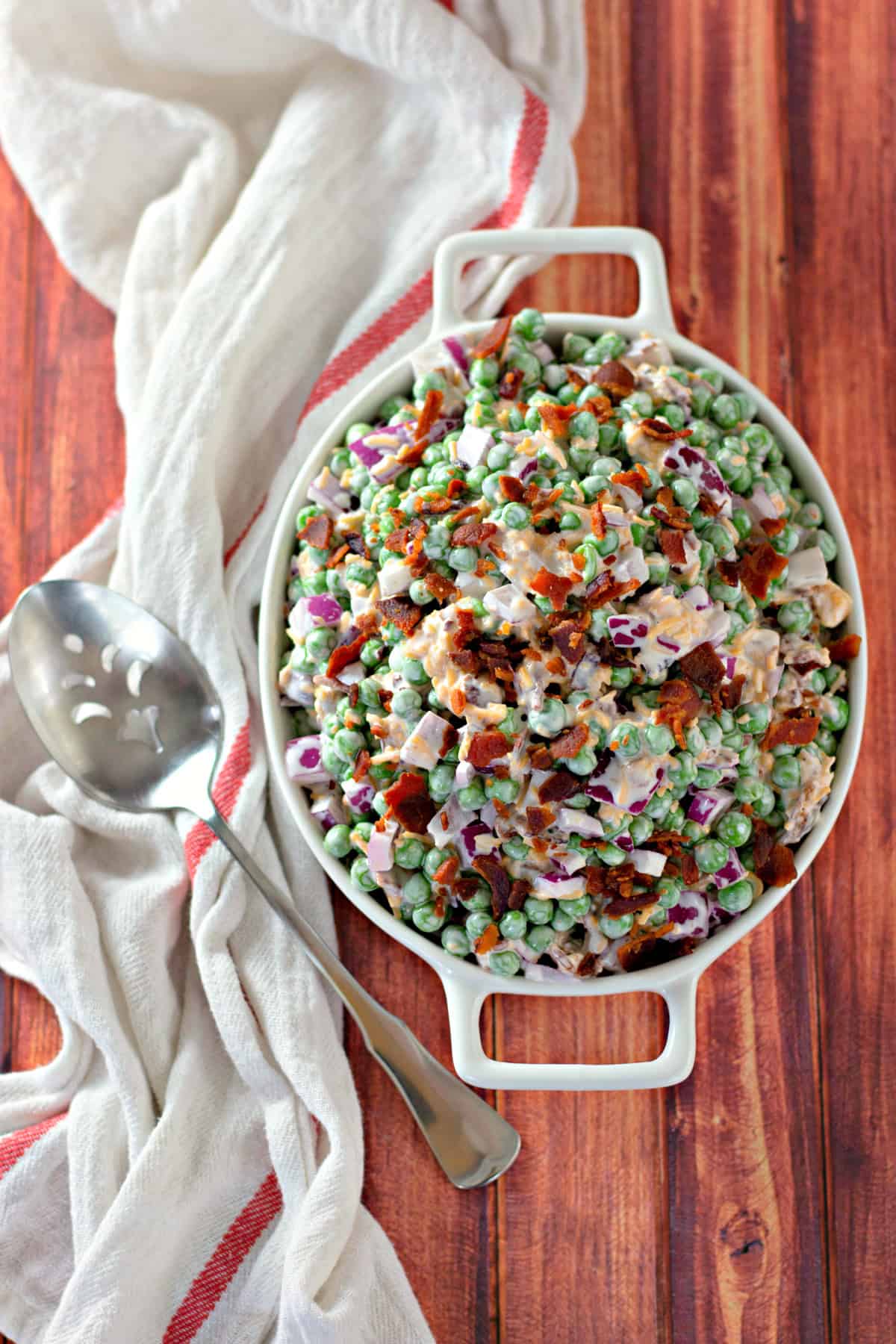 serving bowl with pea salad, serving spoon and white towel