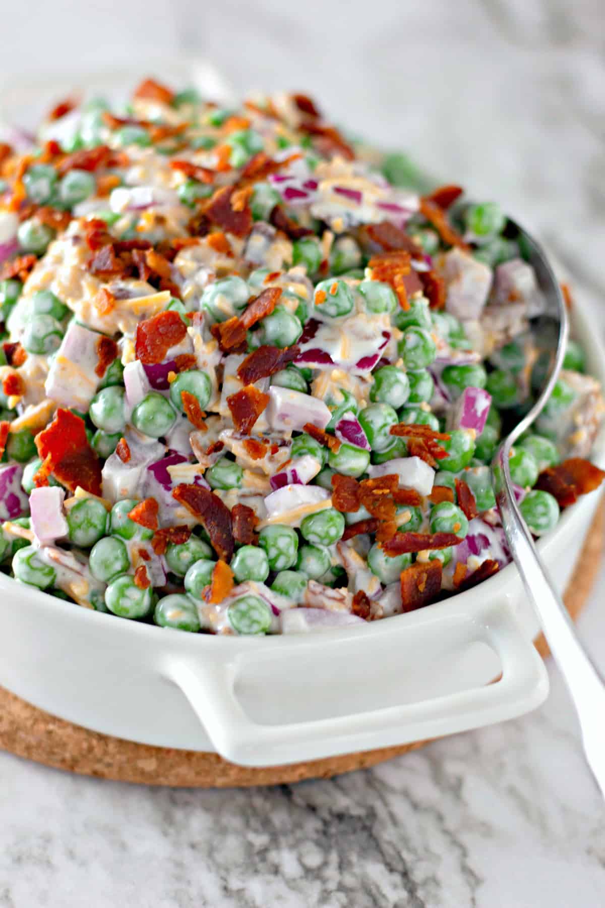 white serving dish with pea salad with serving spoon
