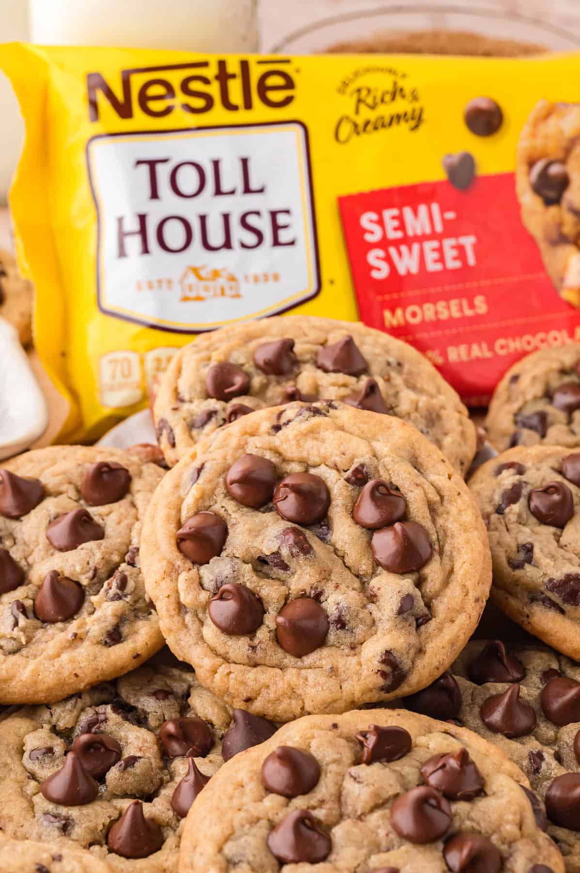 This recipe takes Toll House Chocolate Chip Cookies to the next level with a few tweaks to make them thicker, chewier, & more irresistible. Toll House chocolate chip cookies in front of the bag of chocolate chips
