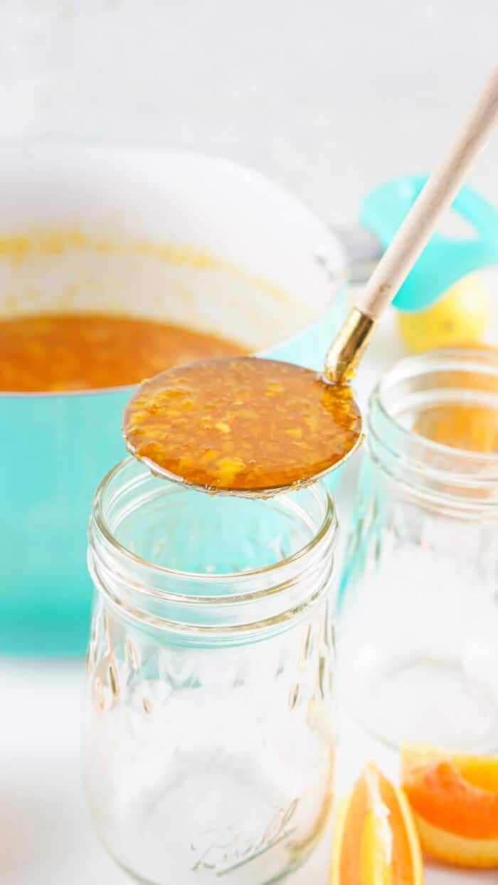 A ladle of orange marmalade above a jar