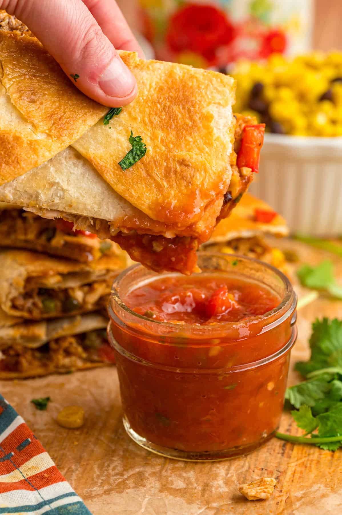 A hand dipping a quesadilla into salsa