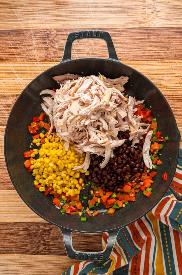 Peppers, shredded chicken, corn, and black beans in a cast iron skillet