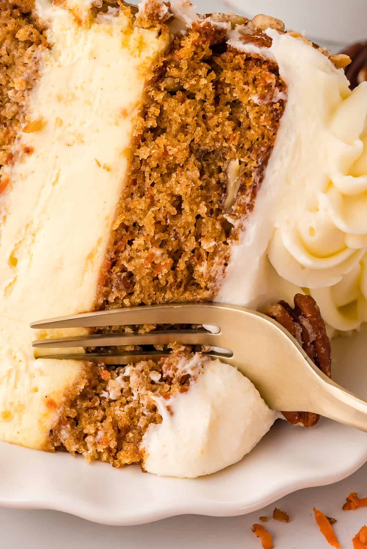 This Carrot Cake Cheesecake features two moist layers of carrot cake and a creamy cheesecake center, topped with cream cheese frosting. A fork cutting into a slice of carrot cake cheesecake