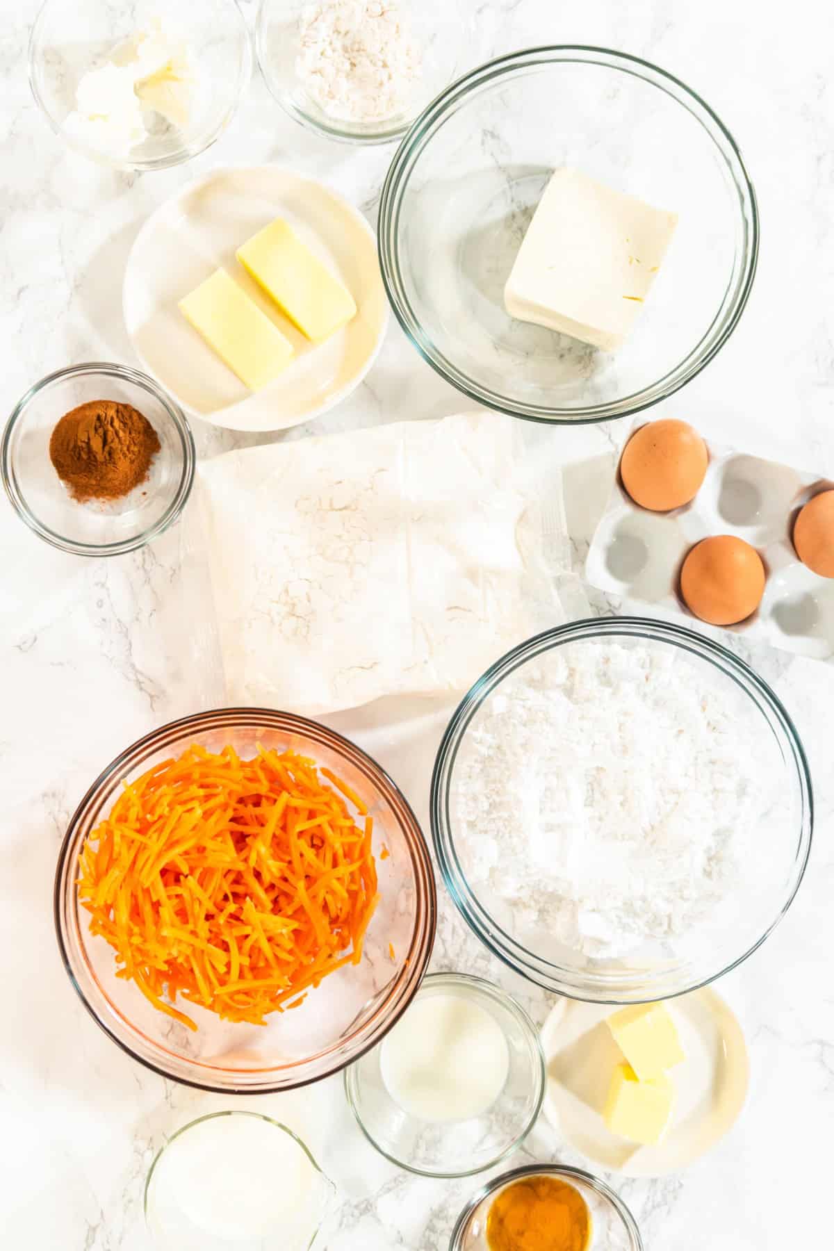 This Carrot Cake Loaf is perfectly moist and tender in the middle, bursting with warm spiced flavors and plenty of fresh carrot goodness. Topped with a rich and tangy cream cheese frosting, every slice is pure comfort and absolutely irresistible! A top-down view of measured ingredients for a carrot cake loaf, including shredded carrots, eggs, butter, flour, sugar, and spices.