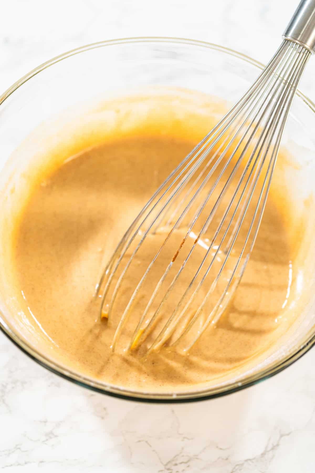 This Carrot Cake Loaf is perfectly moist and tender in the middle, bursting with warm spiced flavors and plenty of fresh carrot goodness. Topped with a rich and tangy cream cheese frosting, every slice is pure comfort and absolutely irresistible! A mixing bowl with smooth, spiced cake batter being whisked.