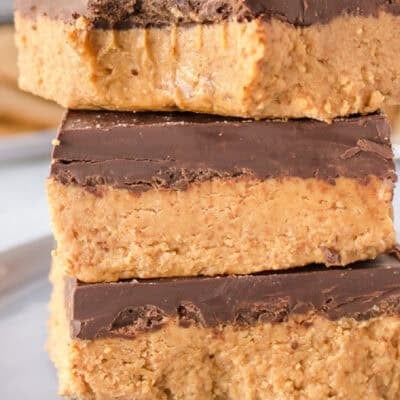 Three stacked no-bake peanut butter bars on a white plate, with the top bar having a bite taken out, revealing its soft interior.