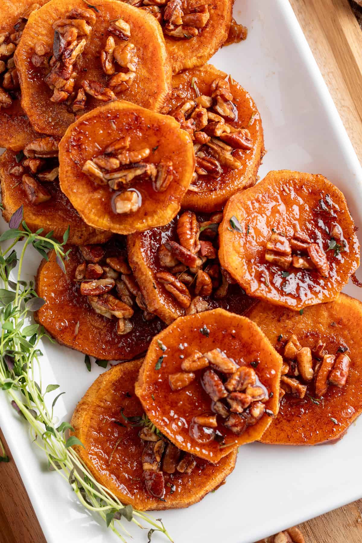These simple Roasted Sweet Potatoes are a flavorful and versatile side dish that pairs perfectly with any meal. They’re caramelized on the outside, tender on the inside, and naturally sweet and buttery—my favorite way to enjoy sweet potatoes! A top-down shot of sweet potato rounds arranged on a white serving dish, caramelized with syrup and pecans.