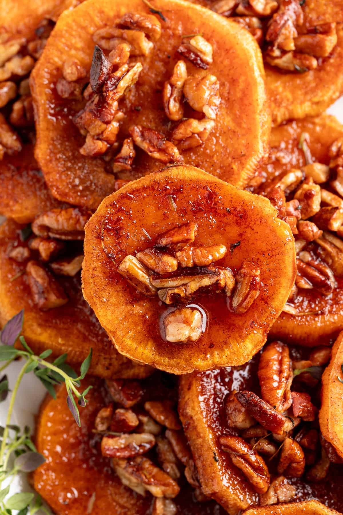These simple Roasted Sweet Potatoes are a flavorful and versatile side dish that pairs perfectly with any meal. They’re caramelized on the outside, tender on the inside, and naturally sweet and buttery—my favorite way to enjoy sweet potatoes! A close-up of syrup-glazed sweet potato rounds topped with toasted pecans, showing the glossy and rich texture.