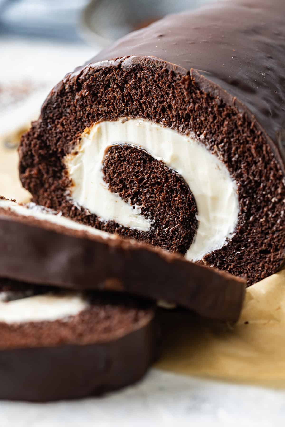 This Swiss Cake Roll features a moist chocolate sponge cake, marshmallow buttercream filling, and chocolate ganache on the outside. A Swiss cake roll with two pieces sliced