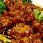 A heaping bowl of Instant Pot orange chicken with broccoli, coated in a shiny orange glaze, served with rice.