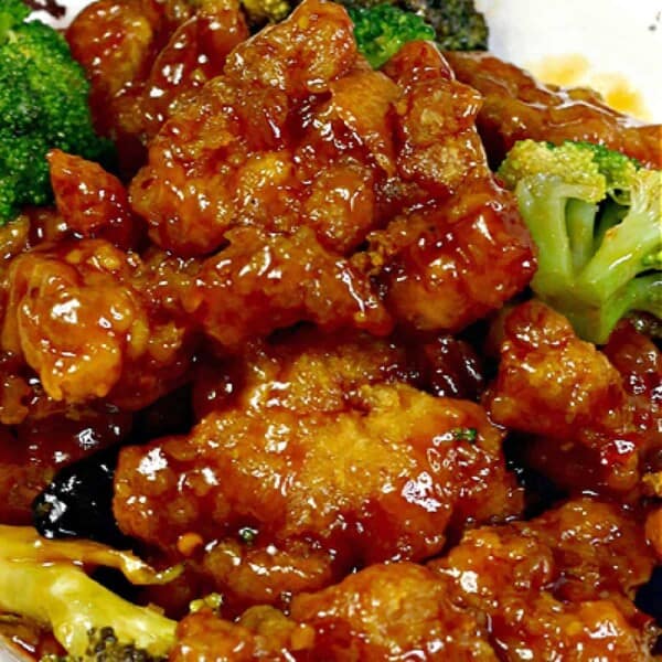 A heaping bowl of Instant Pot orange chicken with broccoli, coated in a shiny orange glaze, served with rice.