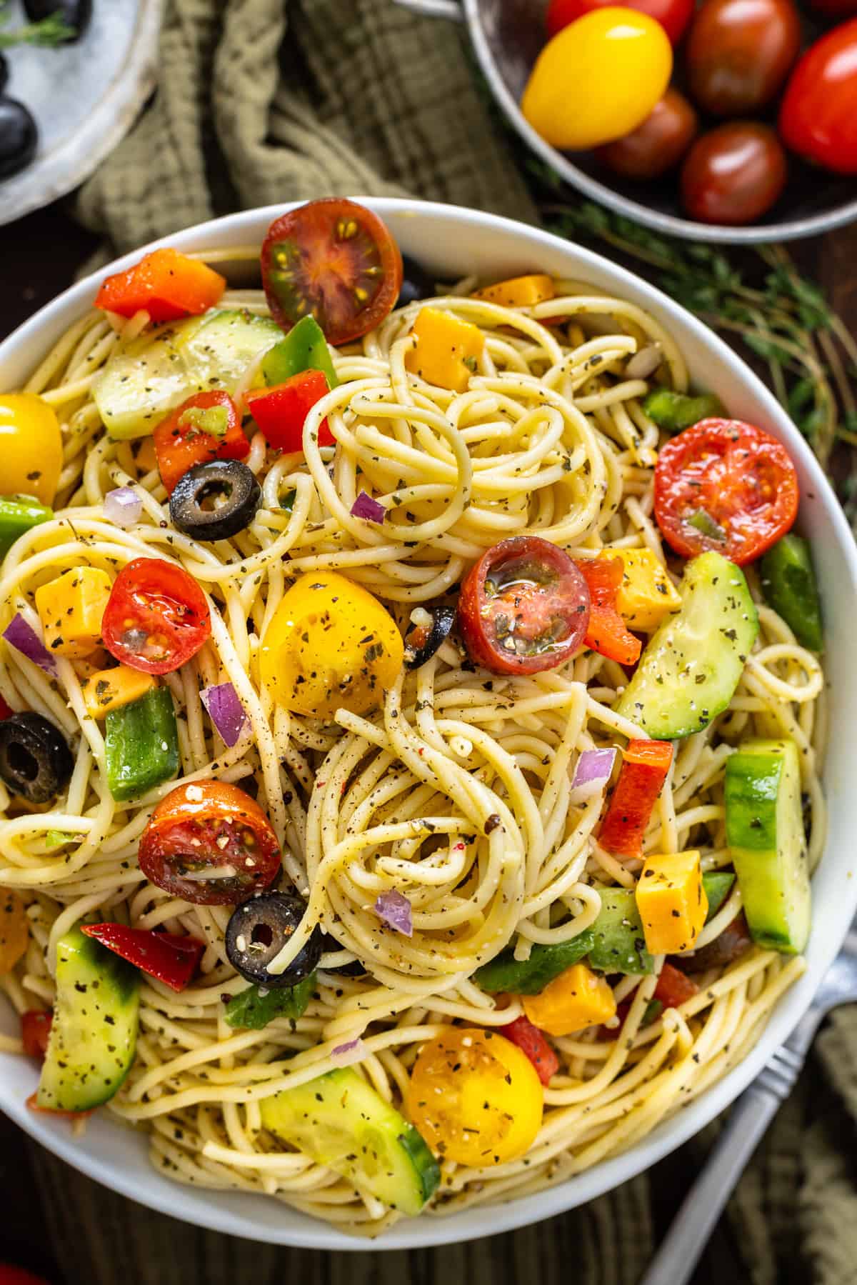 This Spaghetti Salad recipe is loaded with fresh veggies like peppers, tomatoes, and onion plus cheddar cheese and Italian dressing. Overhead view of a bowl of spaghetti salad