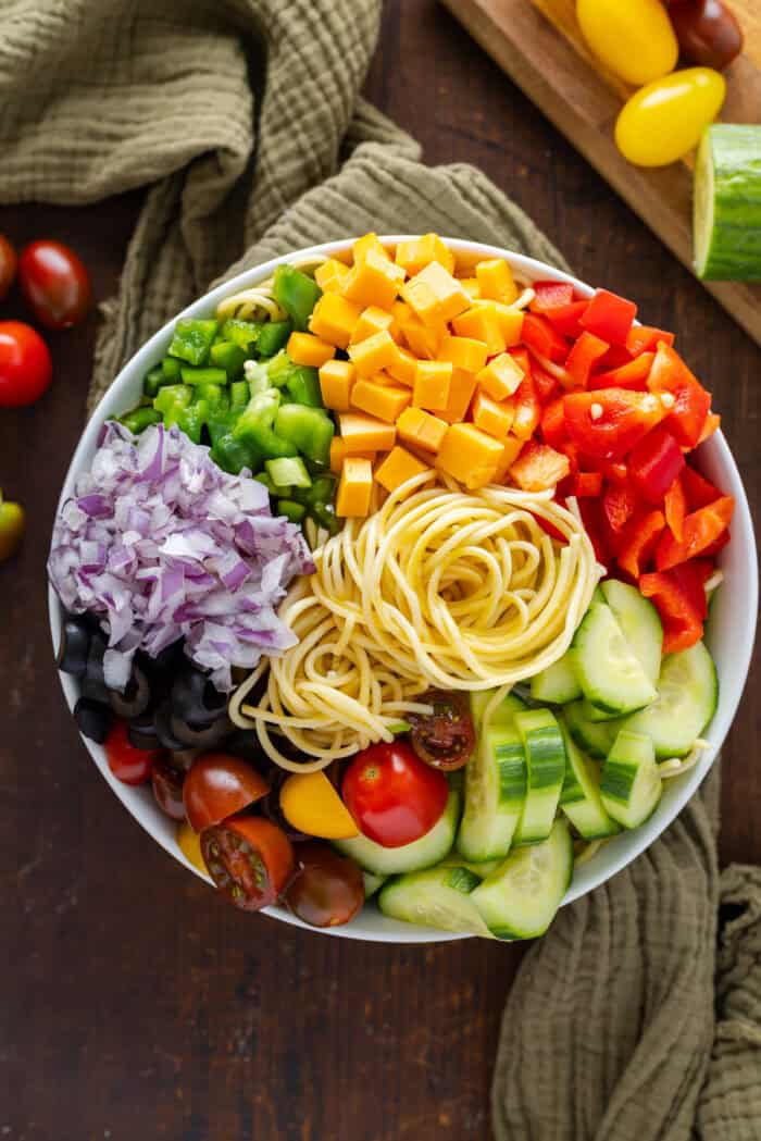 Spaghetti noodles, peppers, onion, olives, tomatoes, and cucumbers in a bowl