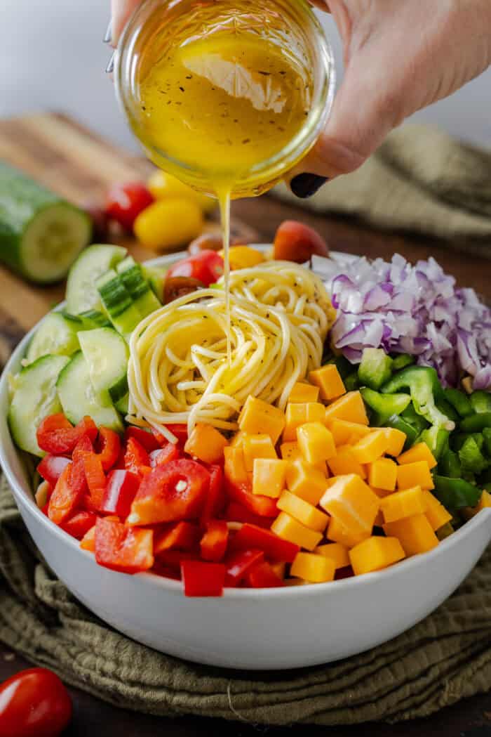 Pouring Italian dressing over a bowl of spaghetti salad ingredients