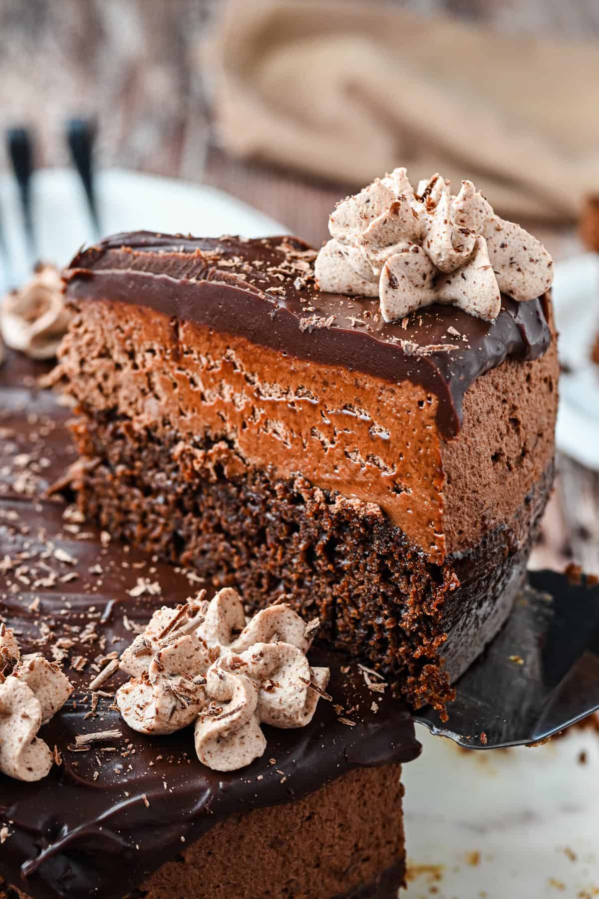 Moist chocolate cake is topped with airy chocolate mousse and rich ganache in this Chocolate Mousse Cake. Easy to make! Serving a slice of chocolate mousse cake