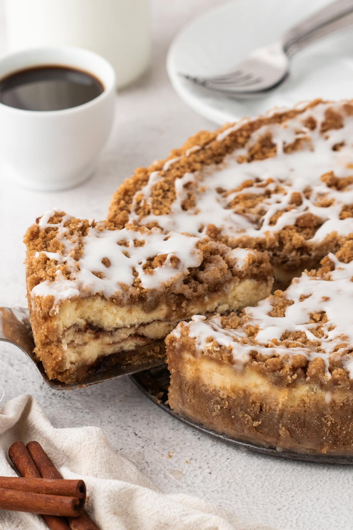 A cake server lifting a slice of coffee cake cheesecake from the whole cheesecake. The slice is thick and layered, with cinnamon swirl and crumb topping, ready to be served.