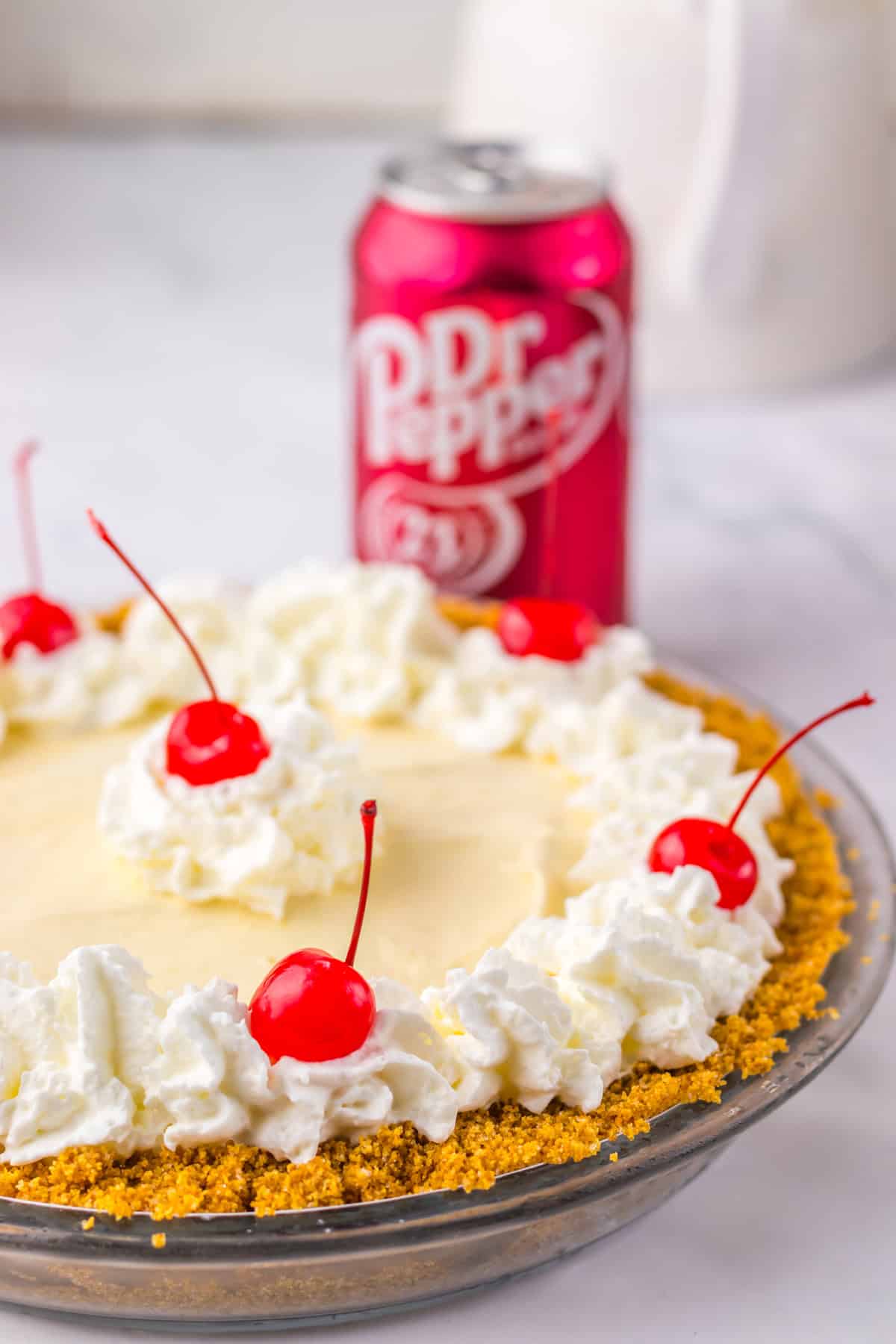 Close-up of Dr Pepper pie garnished with whipped cream and cherries, with a can of Dr Pepper in the background.