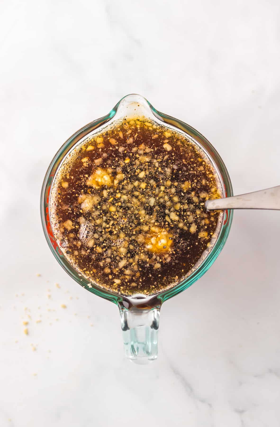 A glass measuring cup filled with a Dr Pepper-based marinade mixture with visible minced garlic and seasonings.