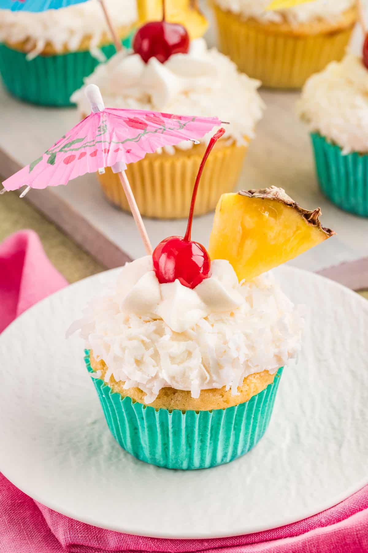 With crushed pineapple, coconut milk, and maraschino cherry juice, these Pina Colada Cupcakes offer a delightful tropical flavor. A pina colada cupcake on a white plate