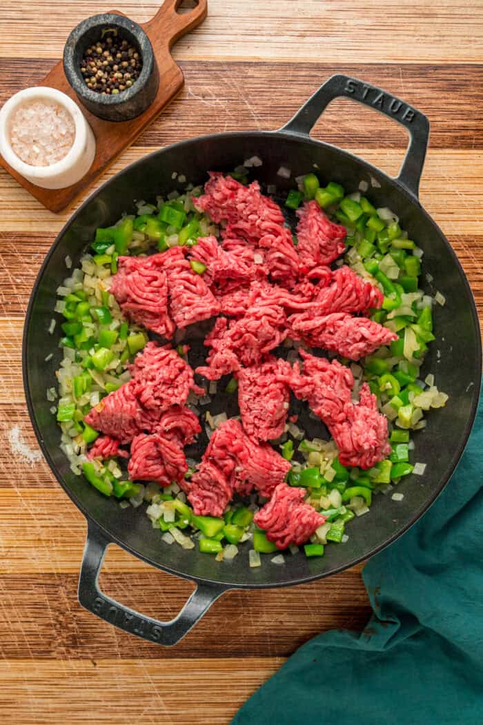 Ground beef in a skillet with diced peppers and onions