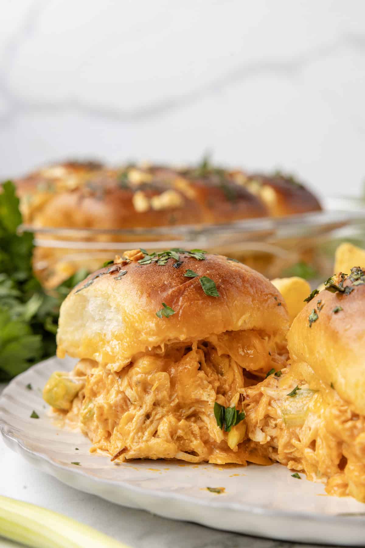 Sweet Hawaiian rolls are topped with spicy buffalo chicken, creamy ranch dressing, and melted cheese in these easy Buffalo Chicken Sliders. A buffalo chicken slider on a plate